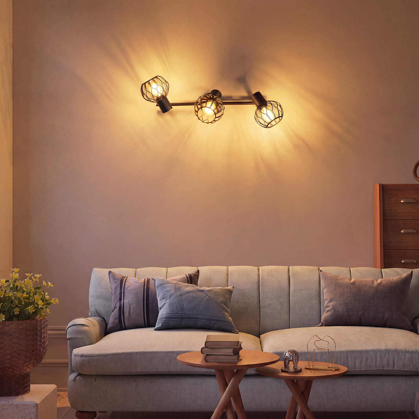 Un sofá gris claro con cojines, dos mesas de madera y lámparas de pared.