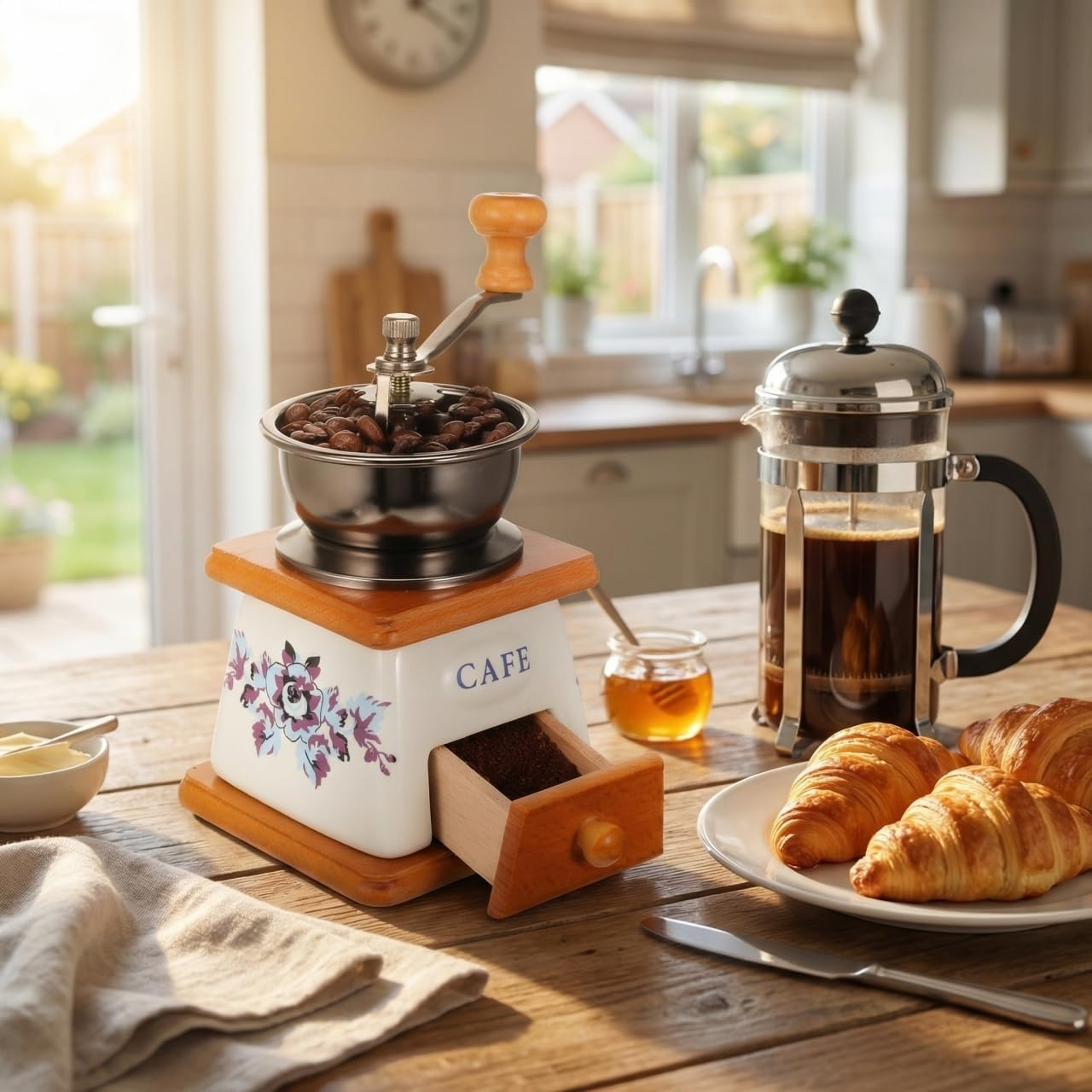Kaffeemühle, French Press, Croissants und Honig auf einem Holztisch.