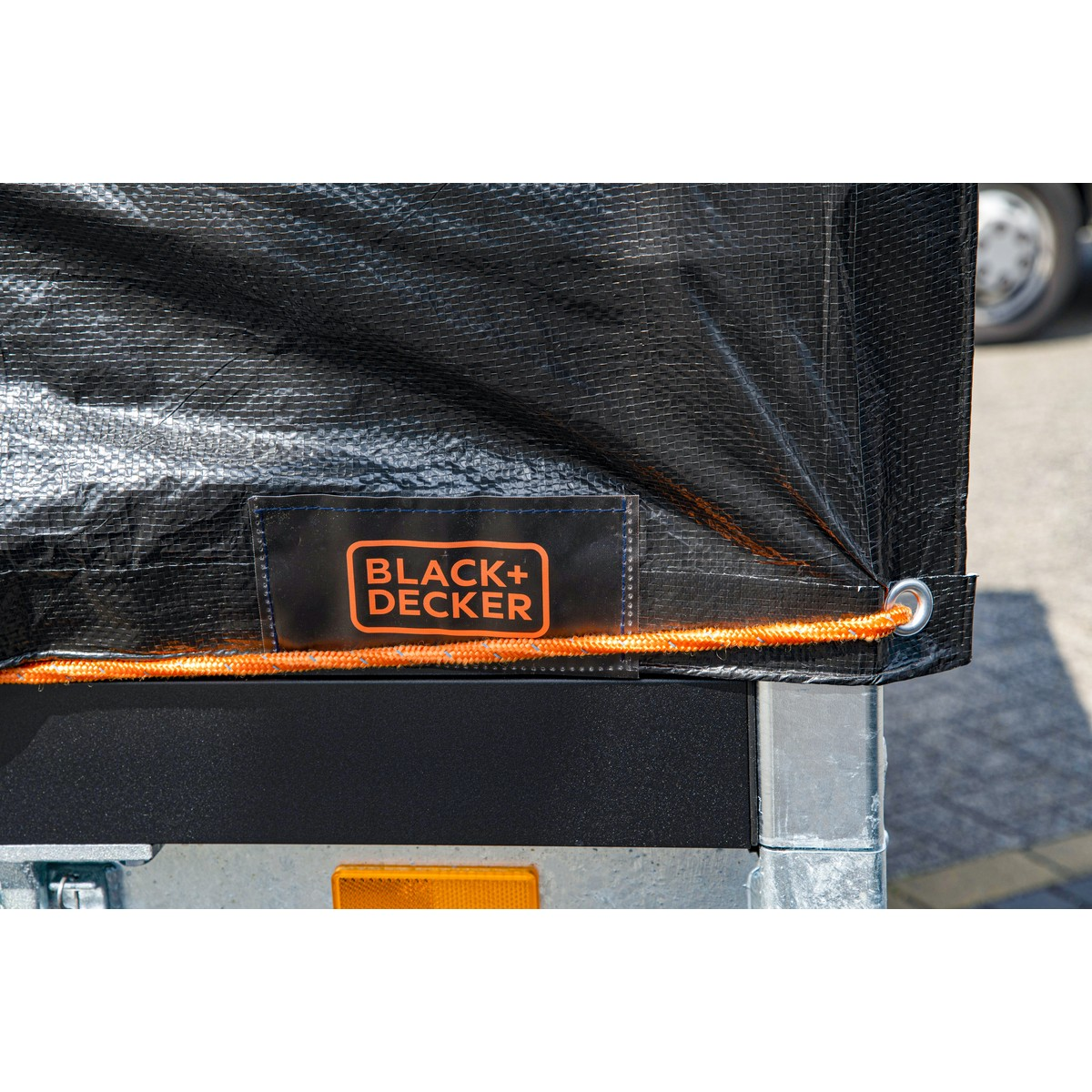 Zwarte tarp met BLACK+DECKER logo en oranje touw op een trailer.
