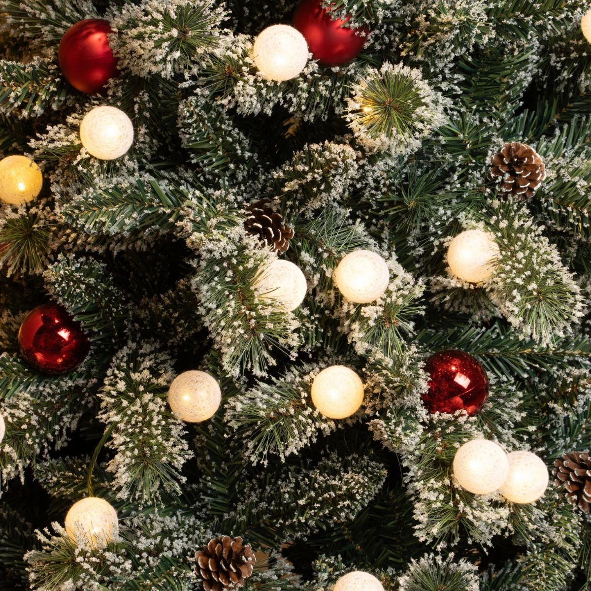A close-up of a frosted Christmas tree with red ornaments and white string lights.