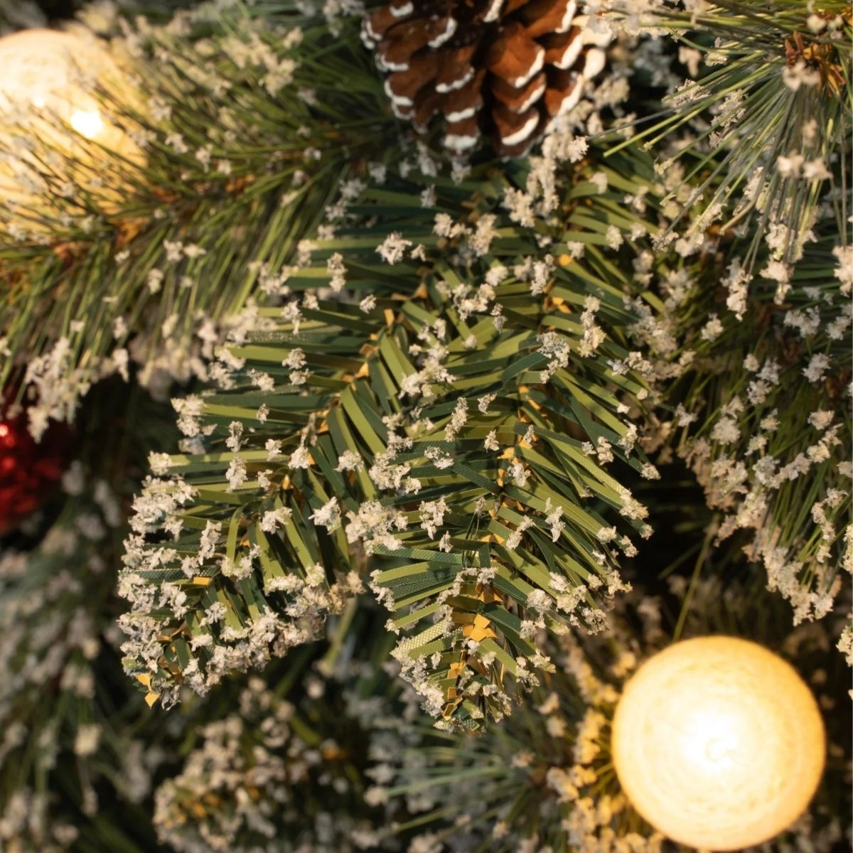 Close-up of a frosted Christmas tree with pinecones and lights.