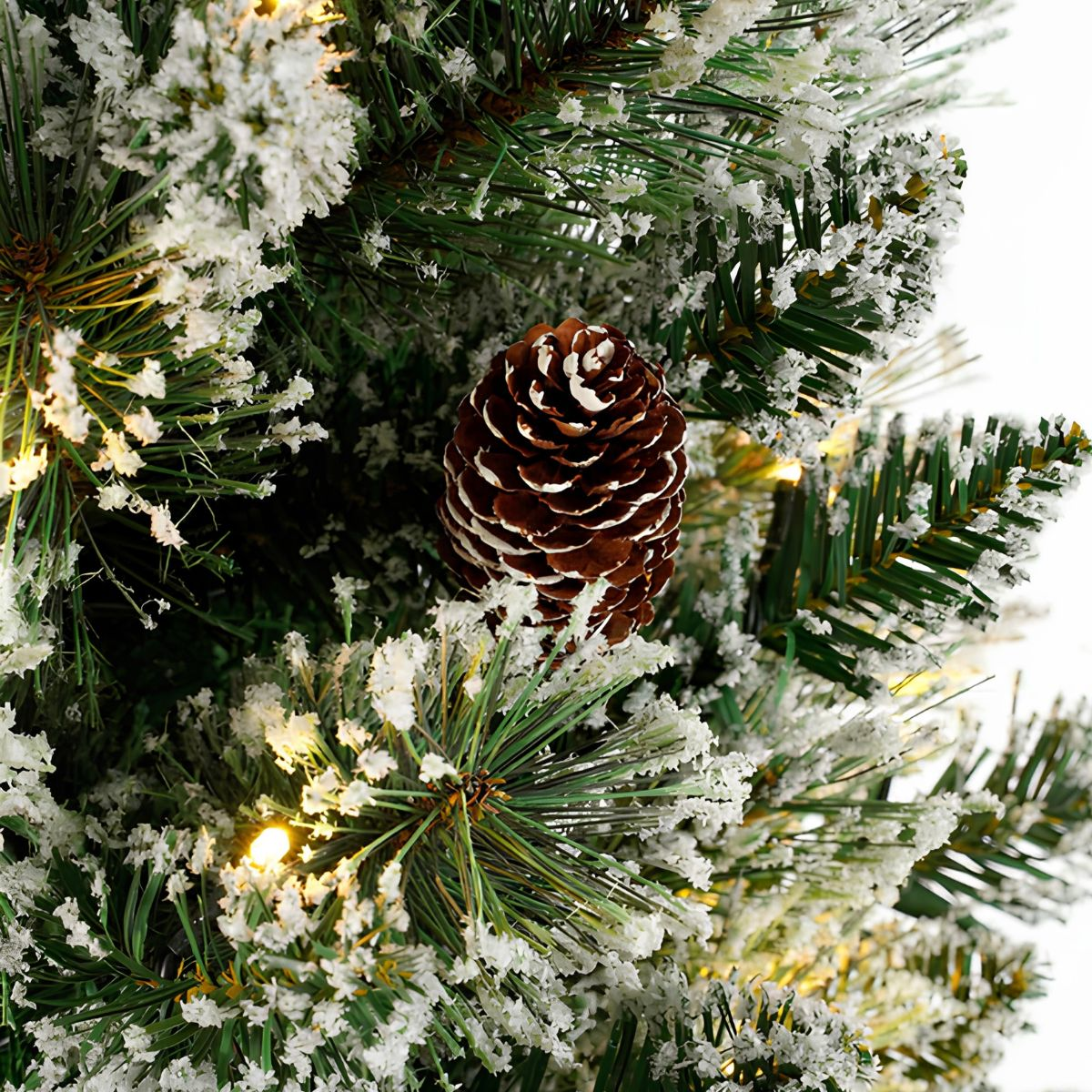 Close-up of a Christmas tree with a pinecone, snow, and lights.