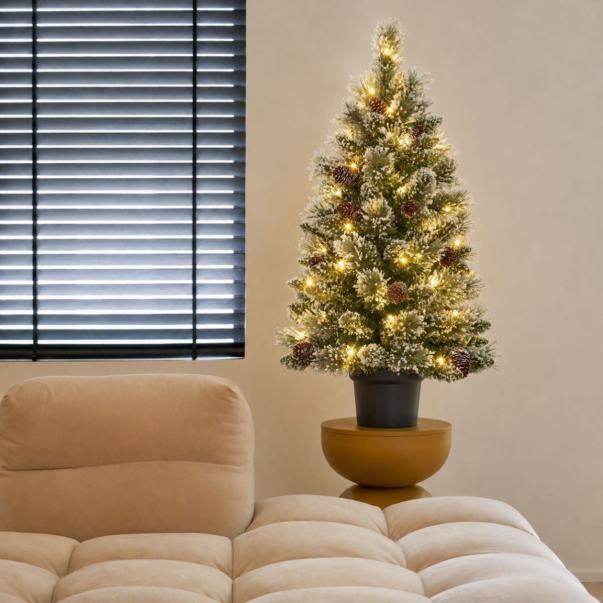 A lit Christmas tree with pinecones sits beside a beige sofa.