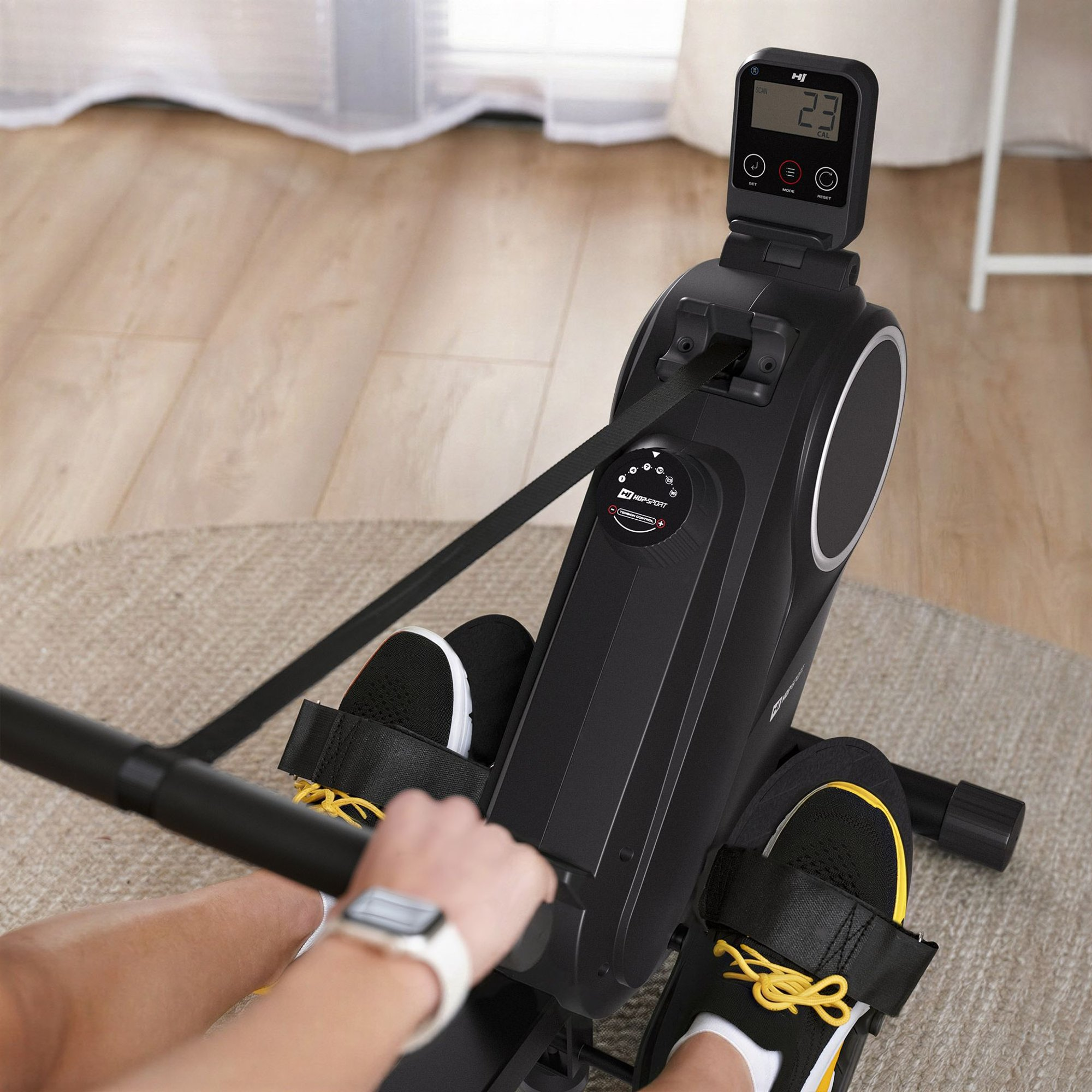 Eine Person benutzt ein schwarzes Rudergerät mit Digitalanzeige, die '23 CAL' anzeigt.
