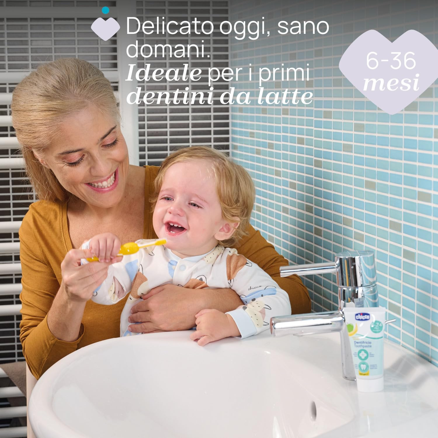 Una donna lava i denti a un bimbo. Sono visibili rubinetto e tubetto dentifricio.