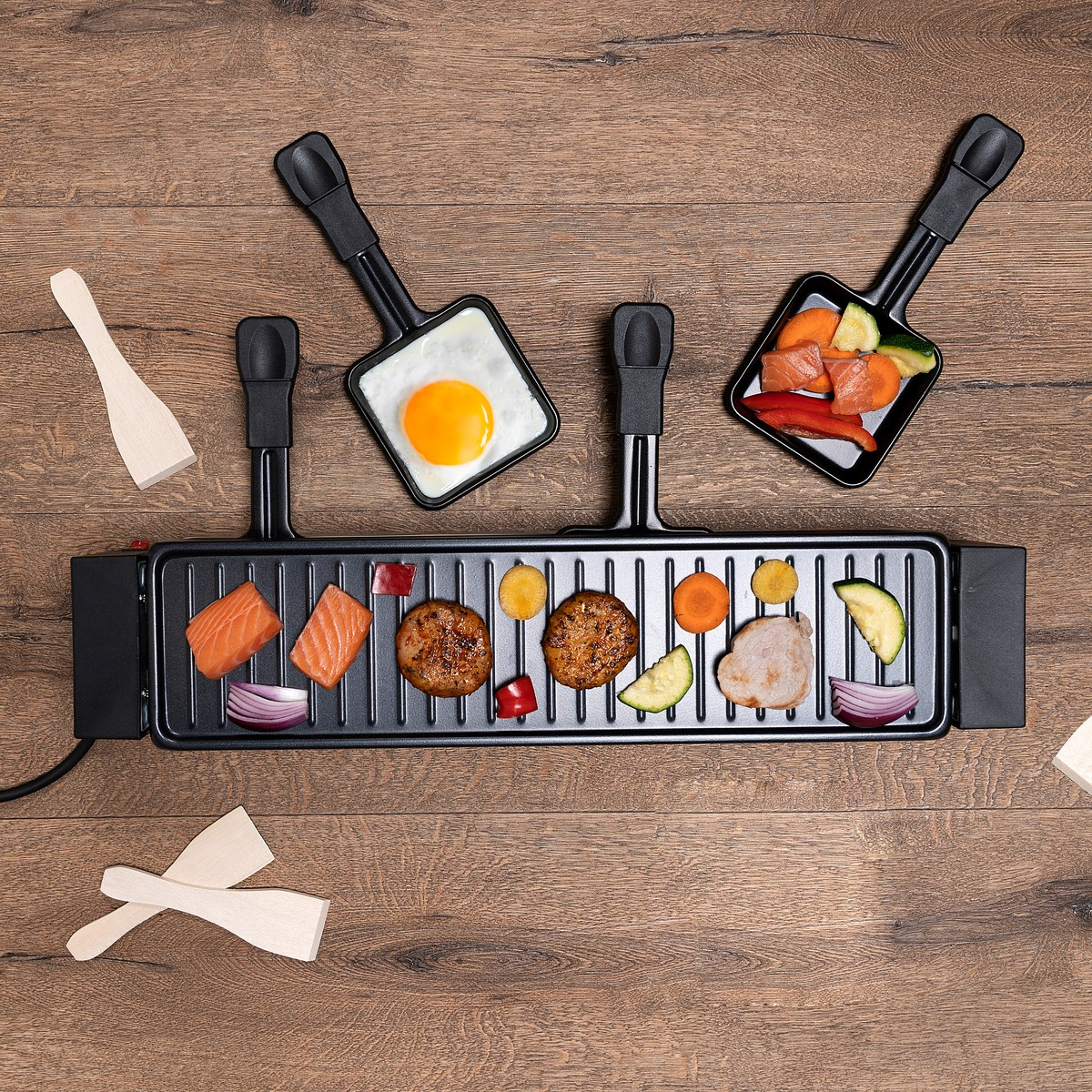 A raclette grill with meat, fish, vegetables, and a fried egg on a wooden surface.