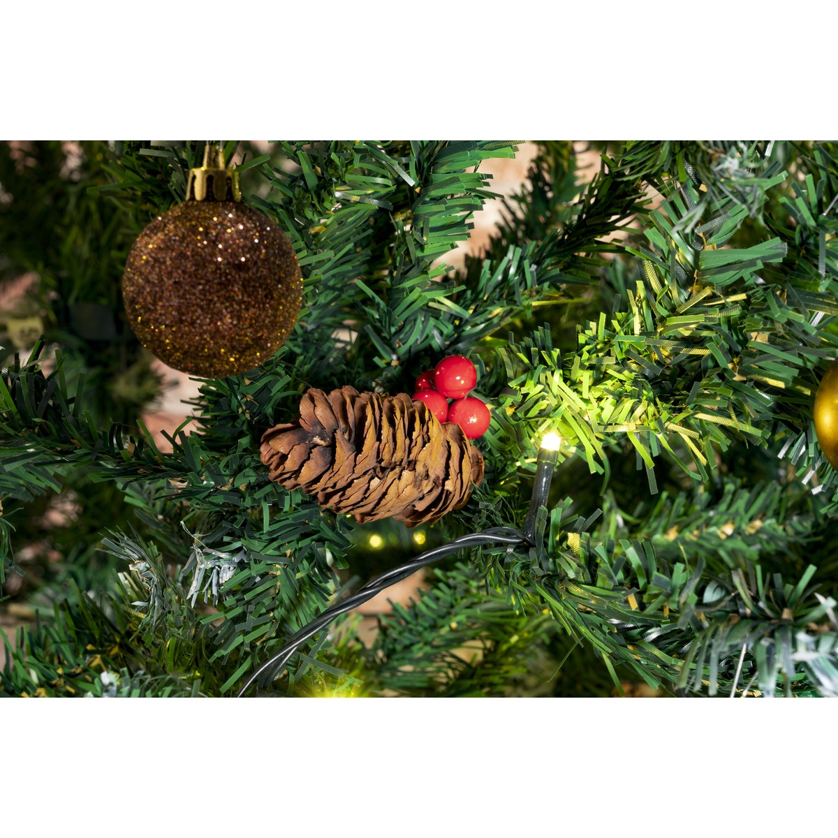 A pinecone with red berries sits on a Christmas tree with a gold bauble.