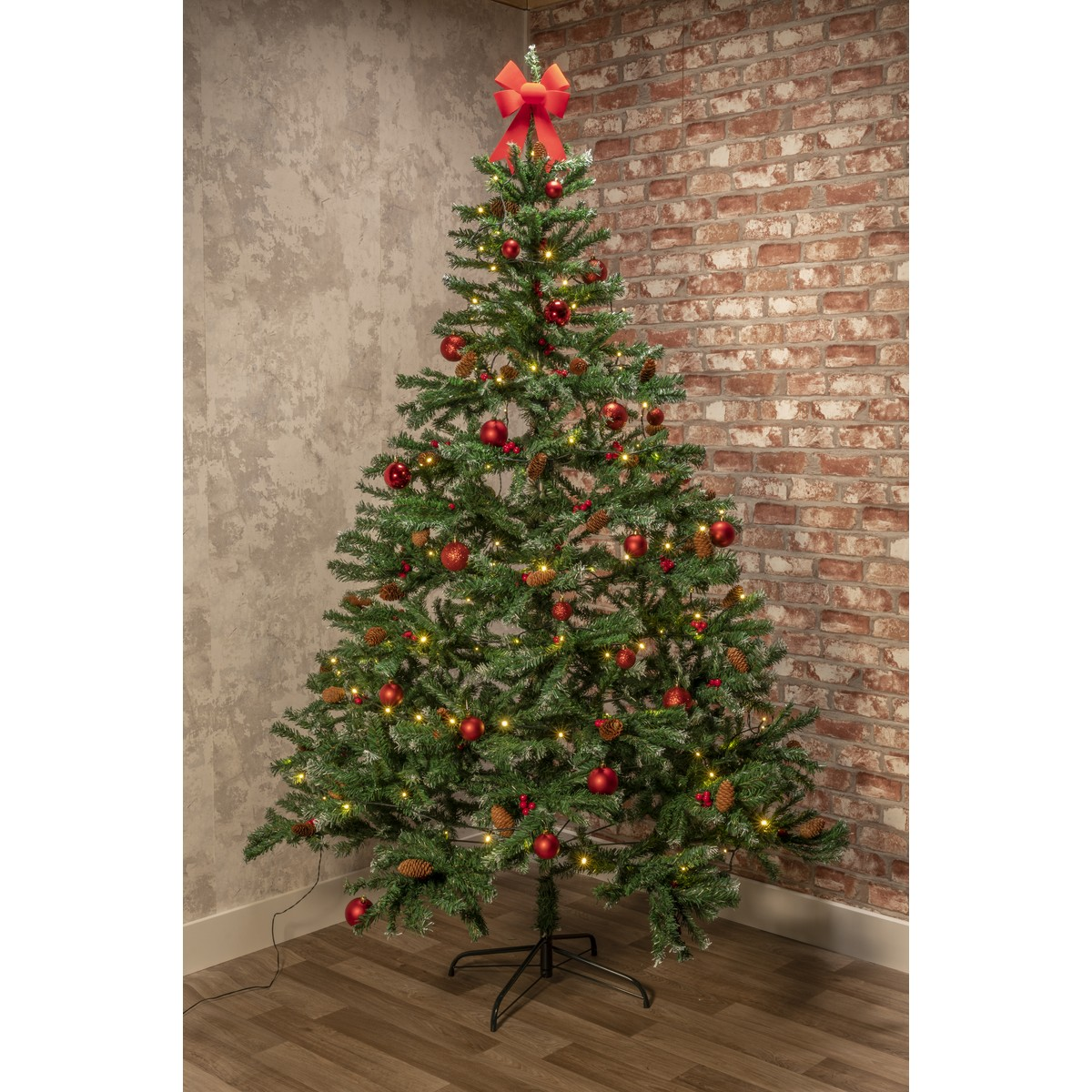 A decorated Christmas tree with red baubles, pinecones and lights, topped with a red bow.