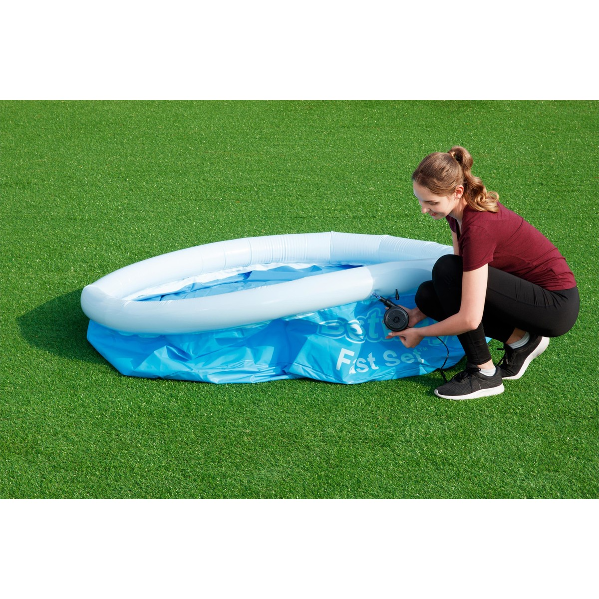 Eine Frau pumpt einen aufblasbaren Pool auf einem Kunstrasenplatz auf.