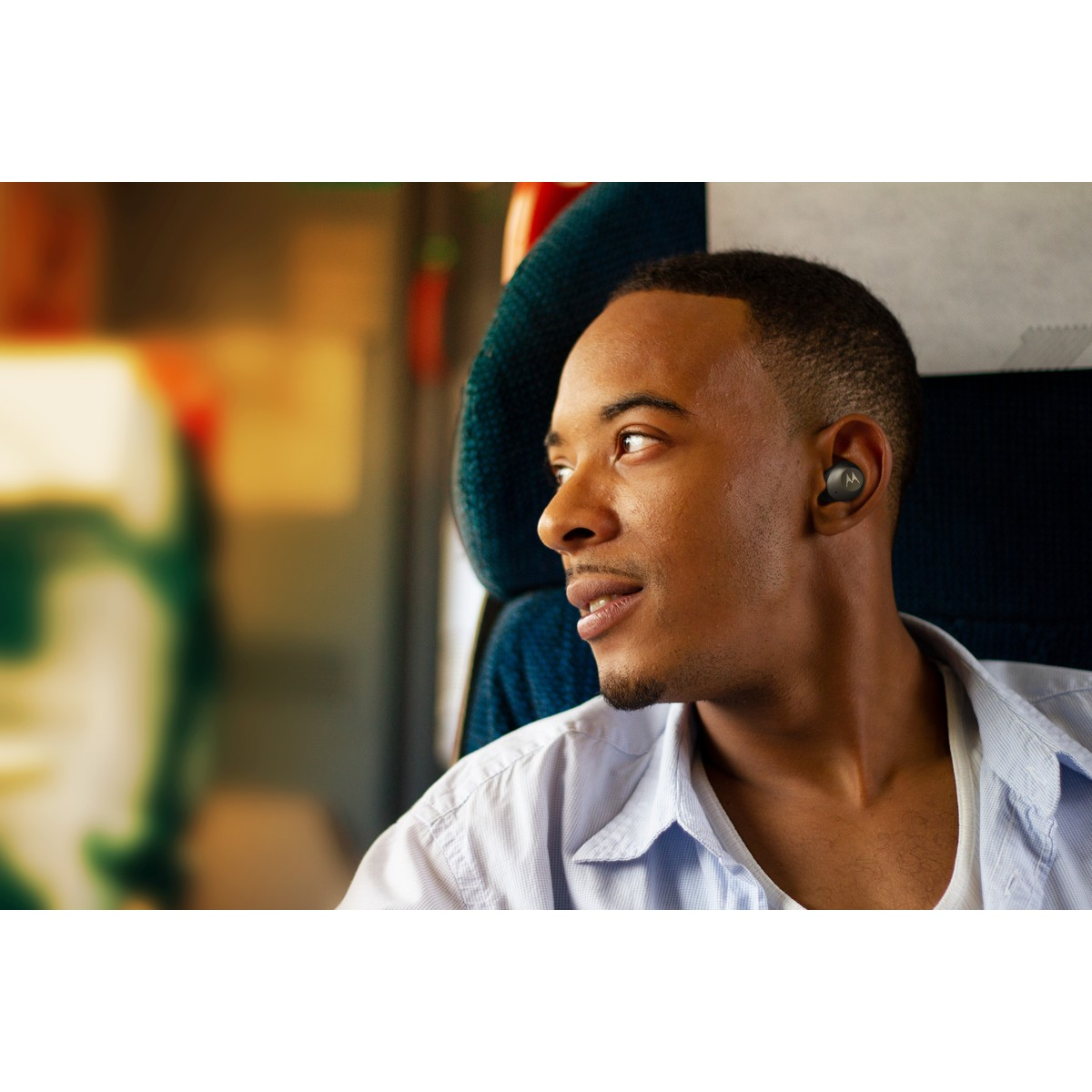 Un hombre con auriculares en un tren mira por la ventana.