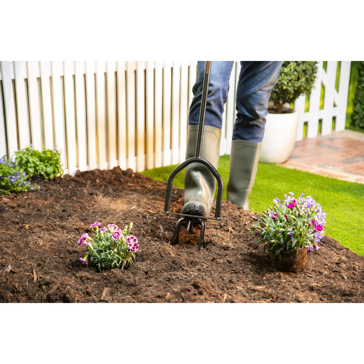 Gardener with tool in soil, planting flowers in front of a fence.
