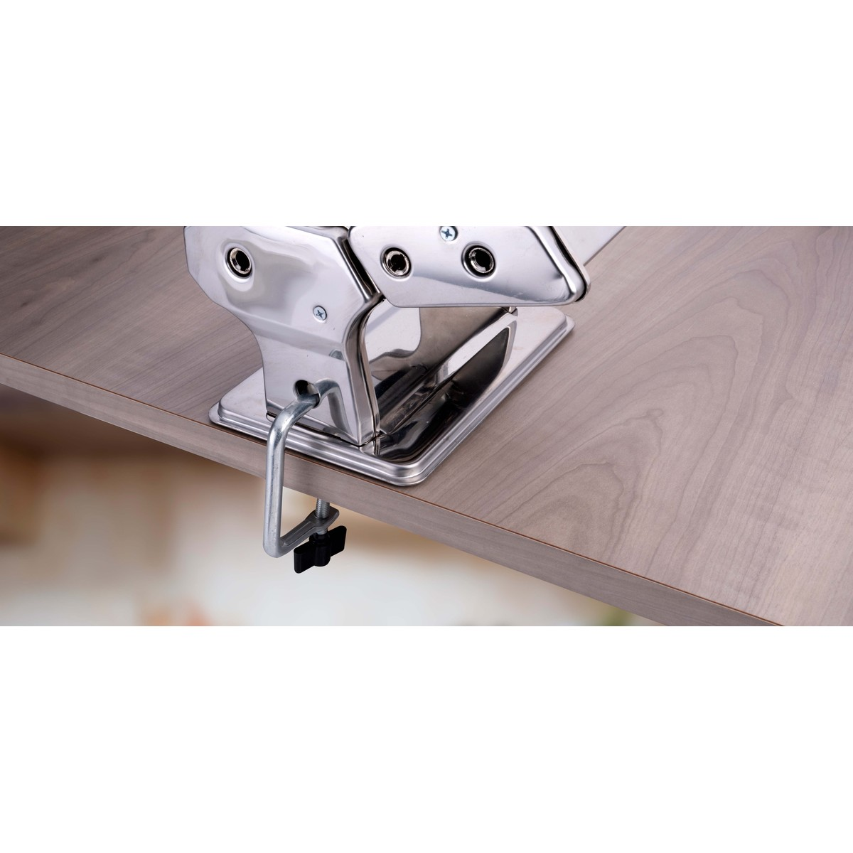 Una macchina per la pasta argentata è fissata su una superficie di legno.