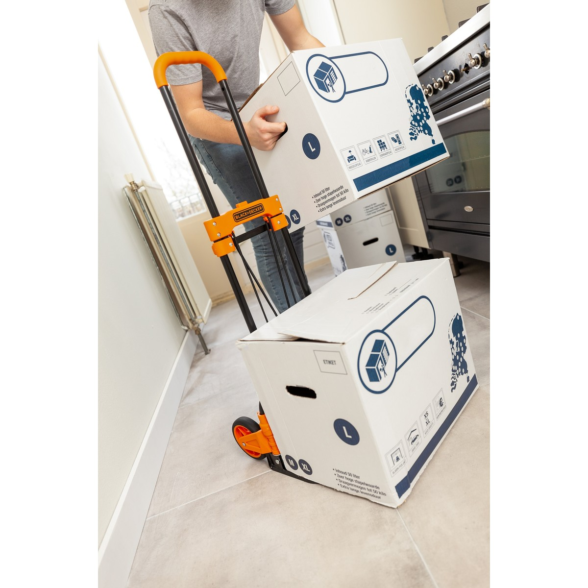 Person with dolly and boxes in hallway, oven nearby.