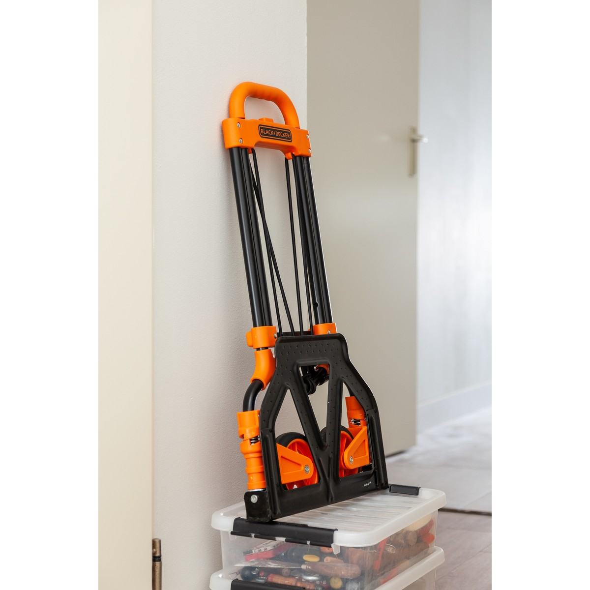 An orange and black dolly rests on a clear bin filled with tools.