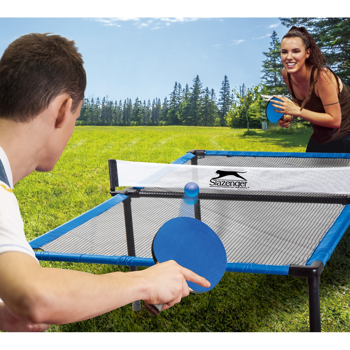 Man and woman playing table tennis outdoors on a blue table.