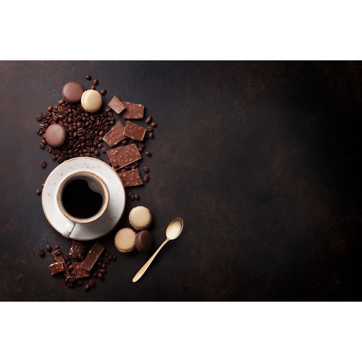 Eine Tasse Kaffee mit Schokolade, Macarons, Kaffeebohnen und einem Löffel auf dunkler Fläche.