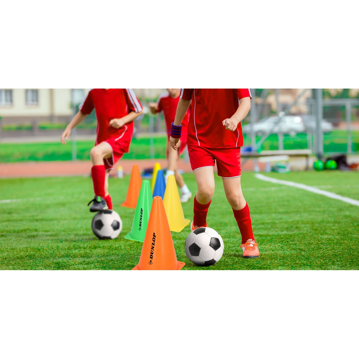 Bambini in tenuta rossa si allenano a calcio su erba sintetica con coni colorati.