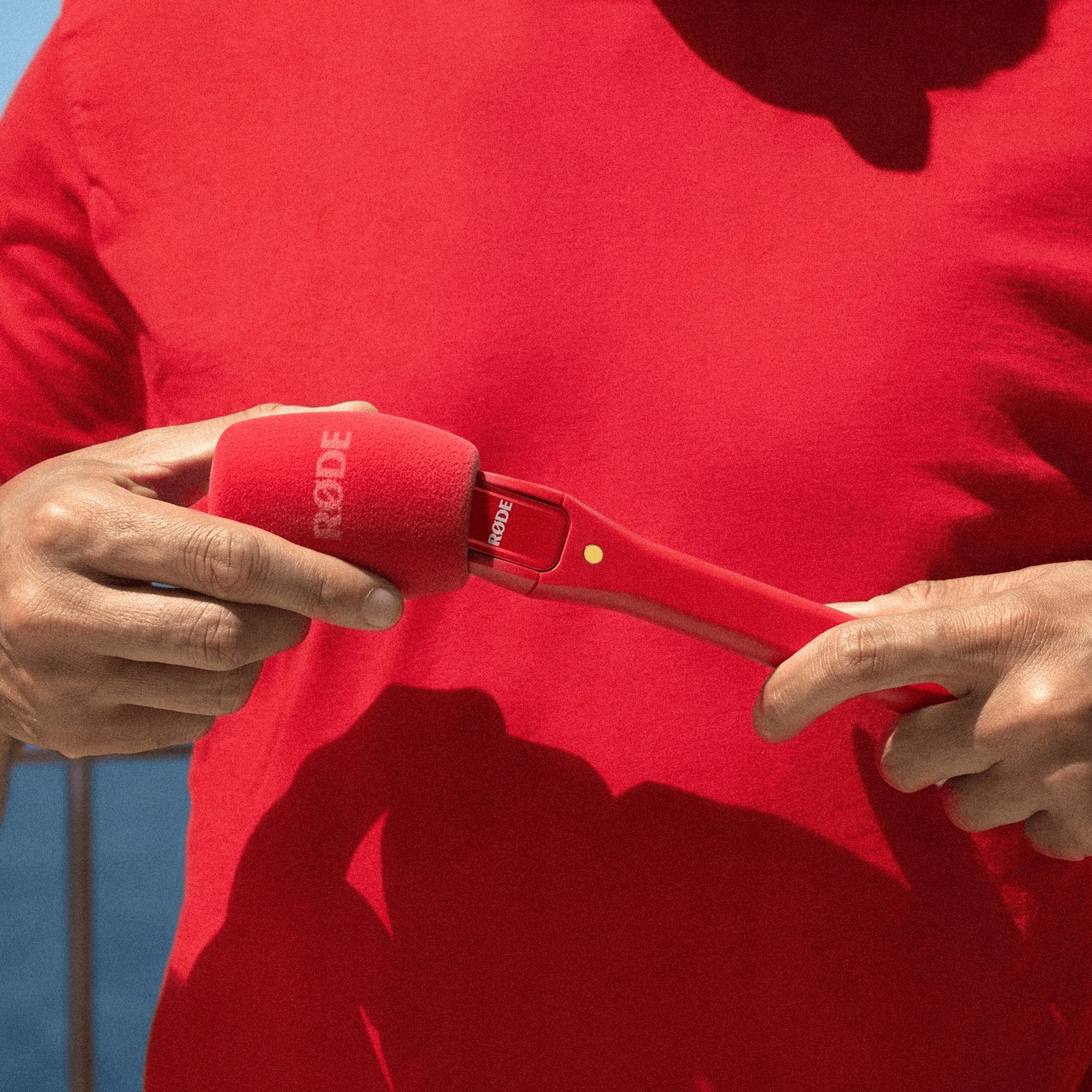 Una persona in camicia rossa tiene un microfono rosso con antivento in schiuma.