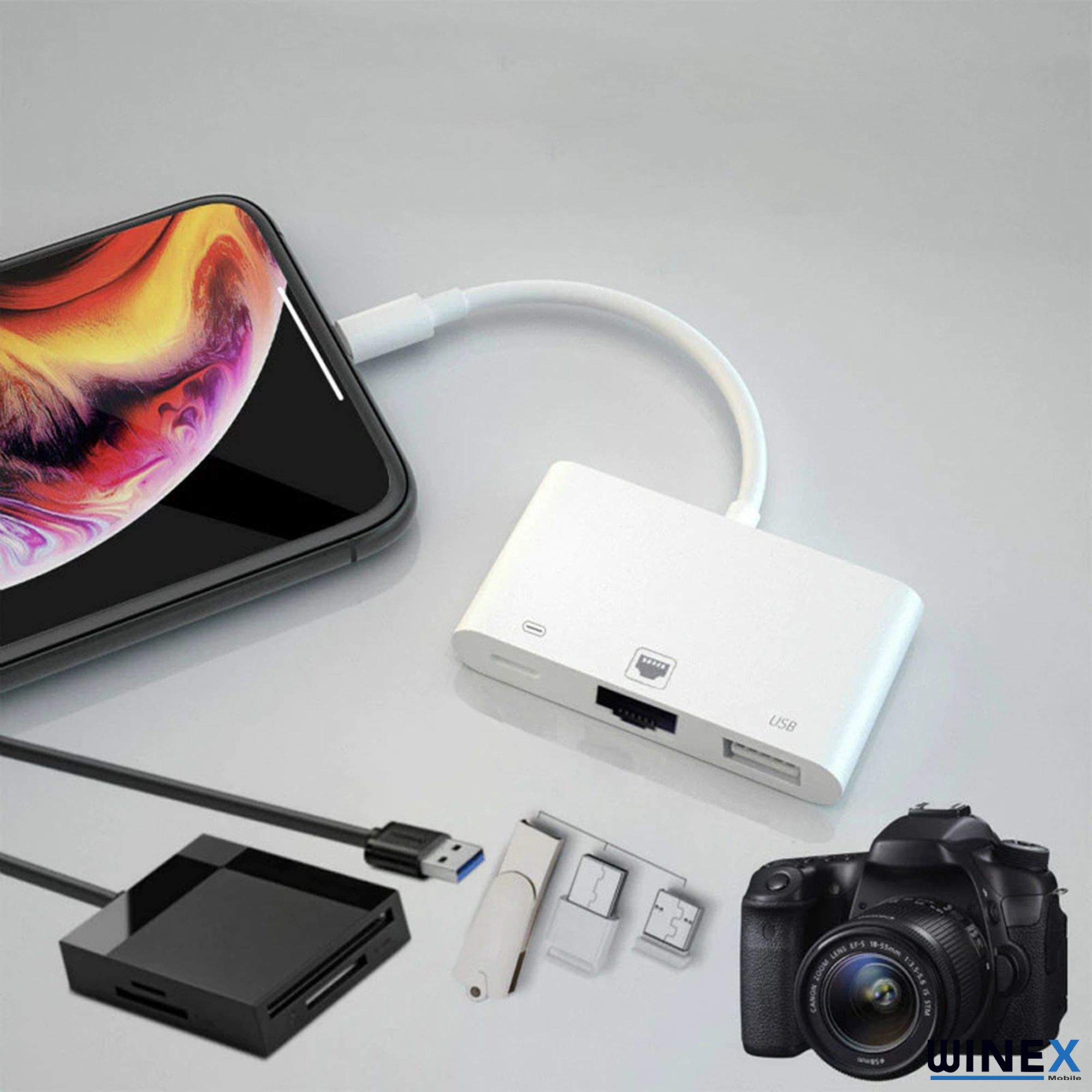 Bir akıllı telefon beyaz bir adaptöre bağlı. Kart okuyucu, USB bellek ve kamera gibi aksesuarlar yanında.