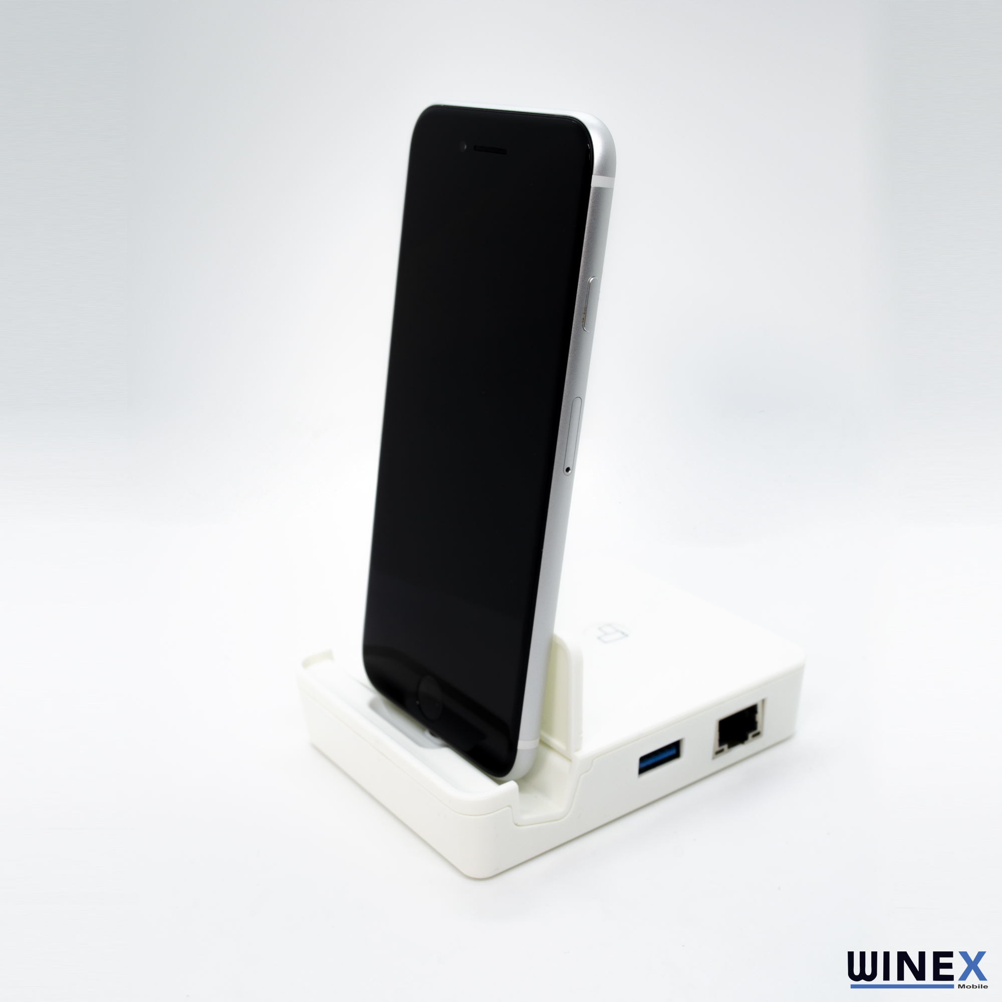 Gümüş renkli bir akıllı telefon, USB ve Ethernet bağlantı noktalarına sahip beyaz bir şarj yuvasında duruyor.
