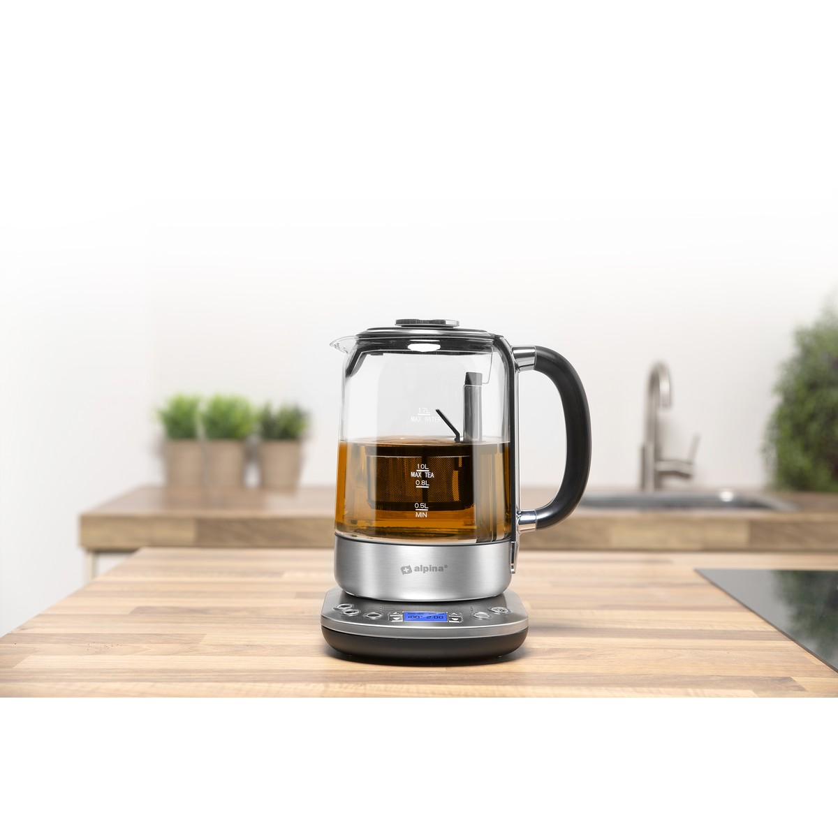 Glas-Teekanne mit Metallbasis auf einer Arbeitsplatte, daneben ein Wasserhahn.