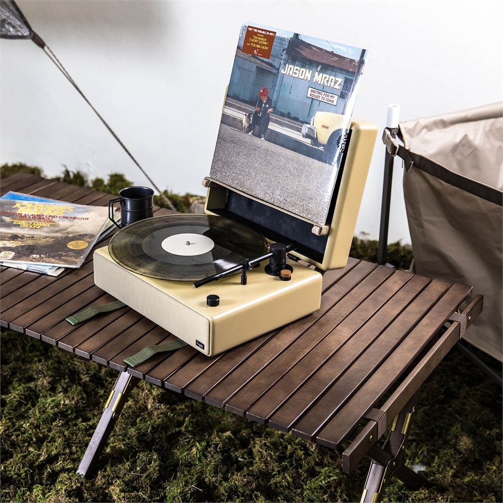 Açık havada ahşap bir masada, vinil plak ve albüm kapağı olan taşınabilir bir pikap.