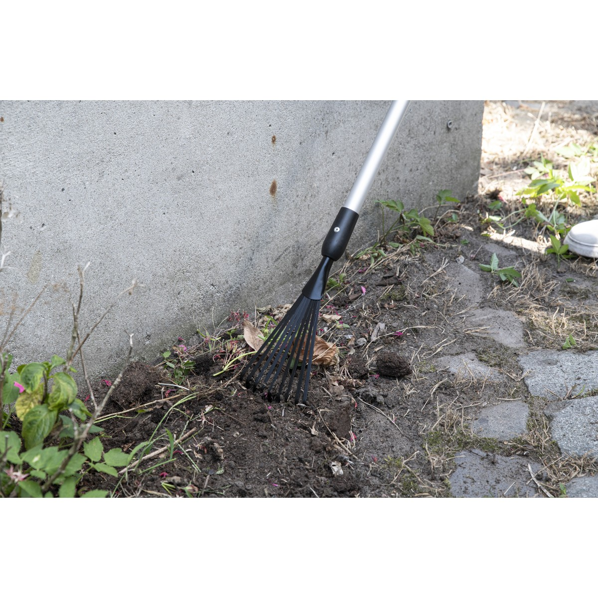 A black rake with a silver handle is used to work the soil and leaves.