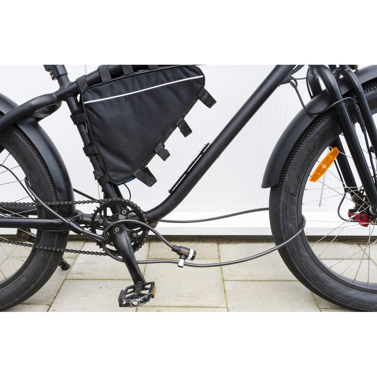 Black bicycle with frame bag, chain, and lock, parked on paving stones.