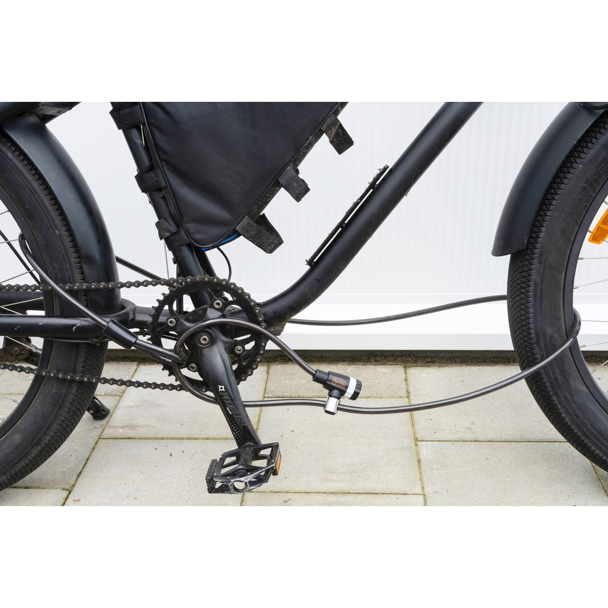 A black bicycle with a cable lock wrapped around the frame and rear wheel.