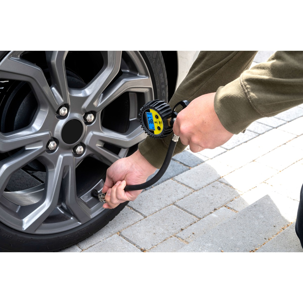 Persoon blaast autoband op met digitale bandenspanningsmeter.