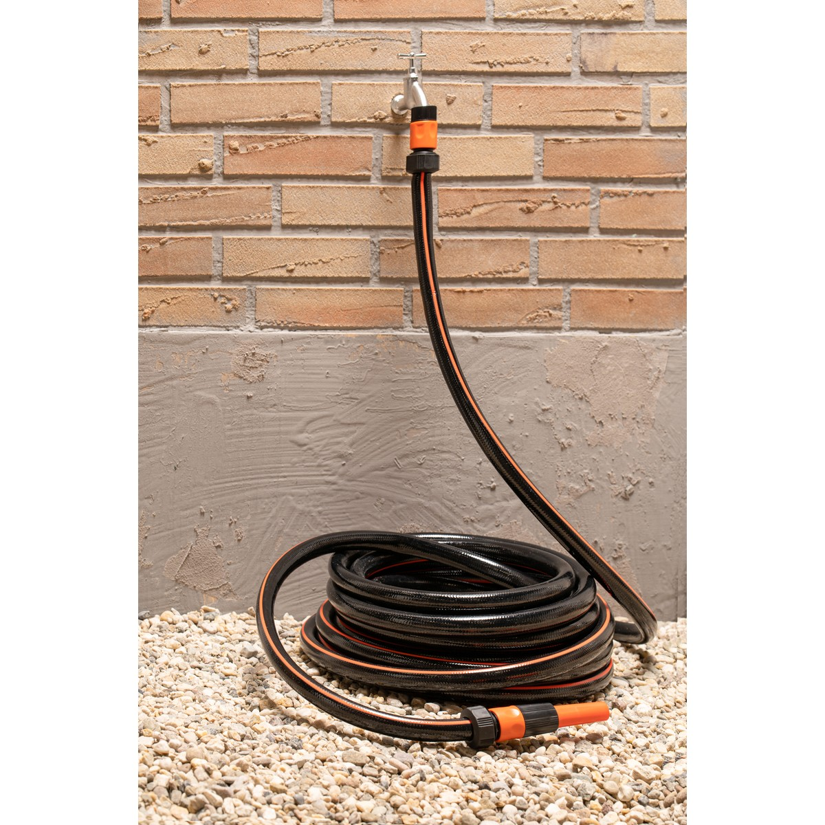 Black garden hose with orange stripes, coiled on gravel, attached to a tap.
