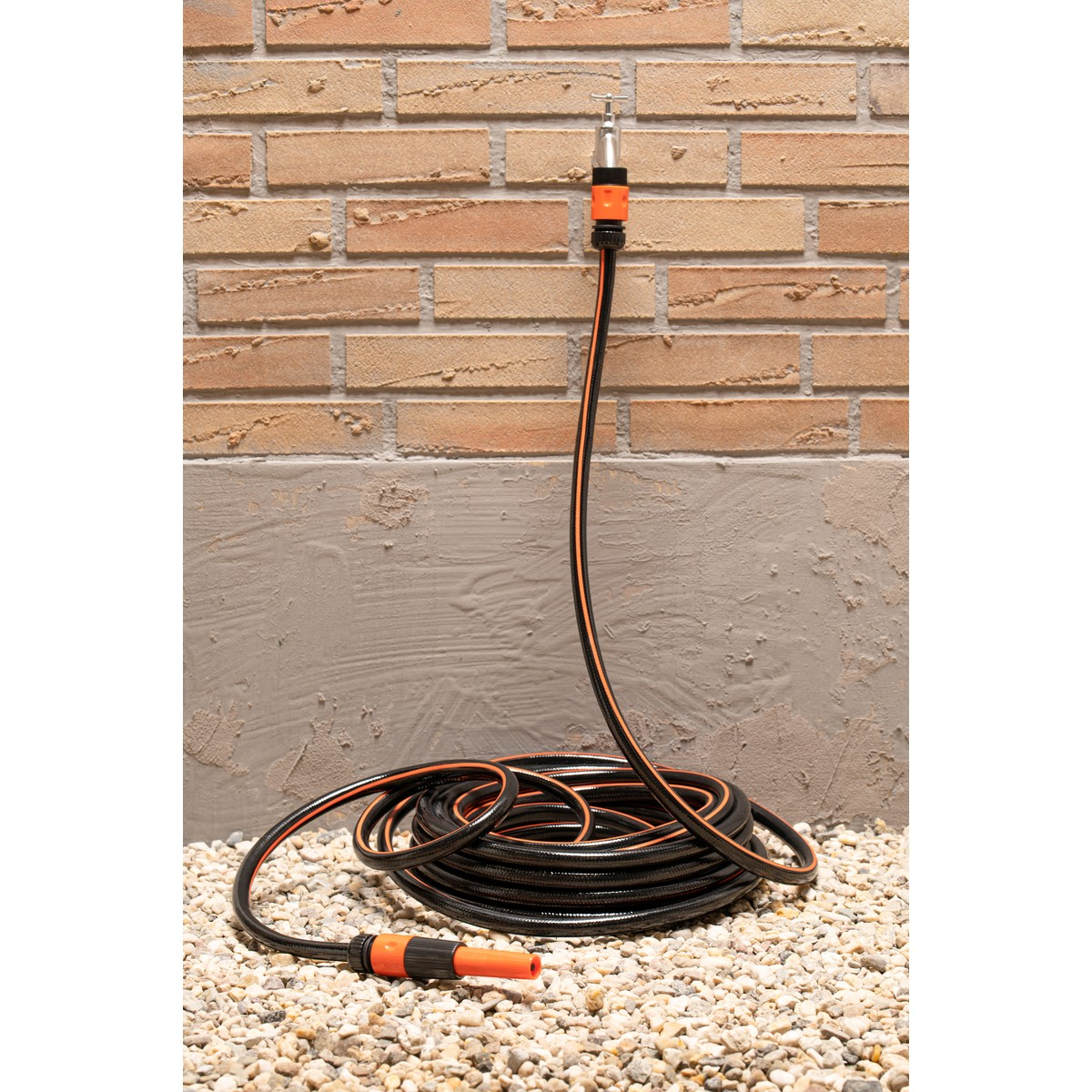 Black garden hose with orange stripes, coiled on gravel.