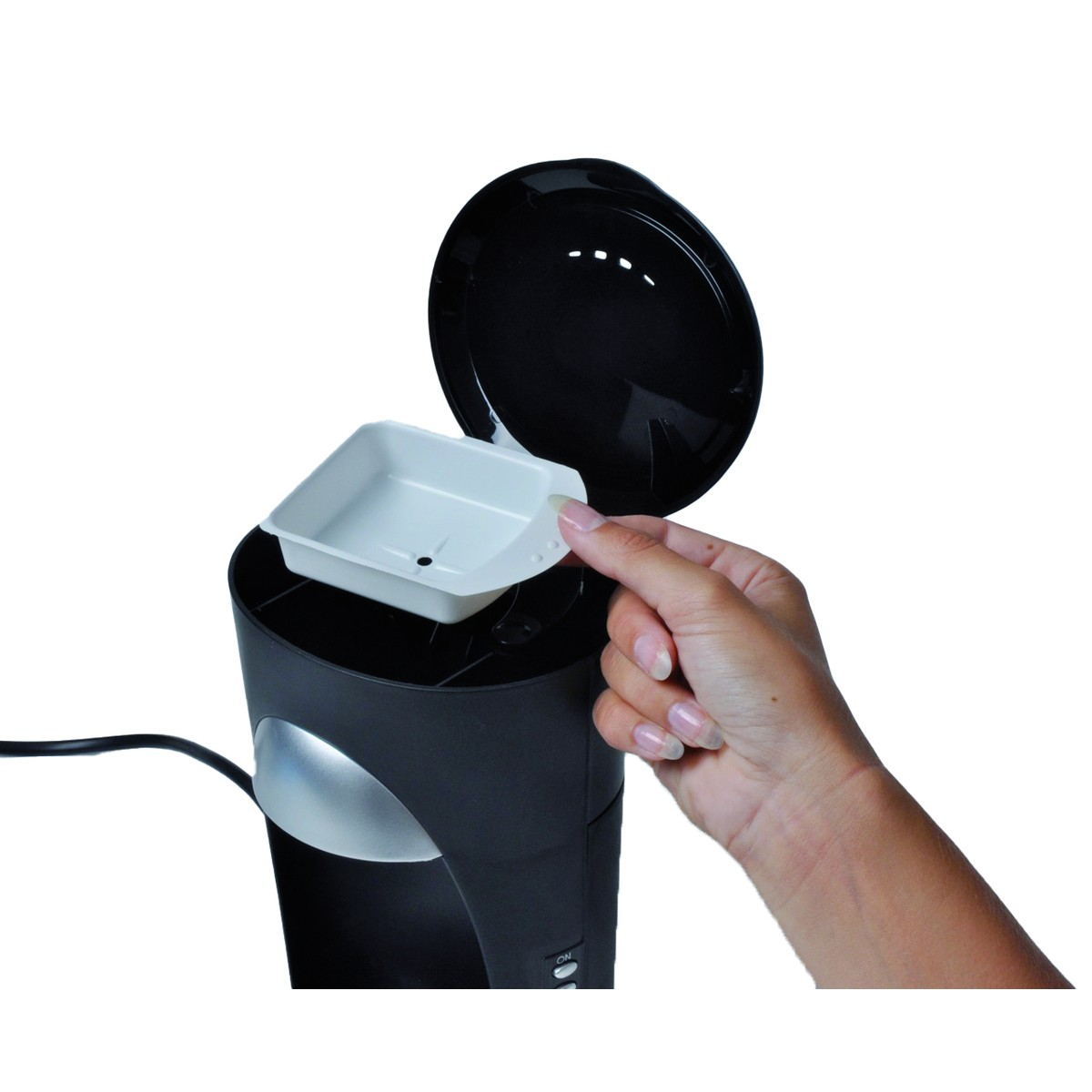 A hand places a white tray into a black device with its black lid open.