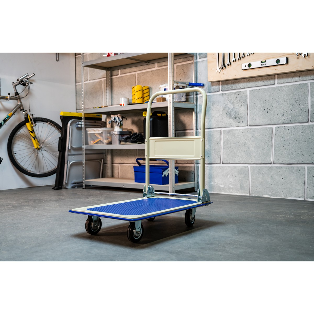 A blue trolley with beige handles sits on a concrete floor, tools in the background.