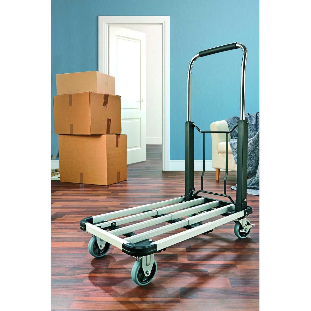 A dolly stands on a wooden floor in front of stacked cardboard boxes.