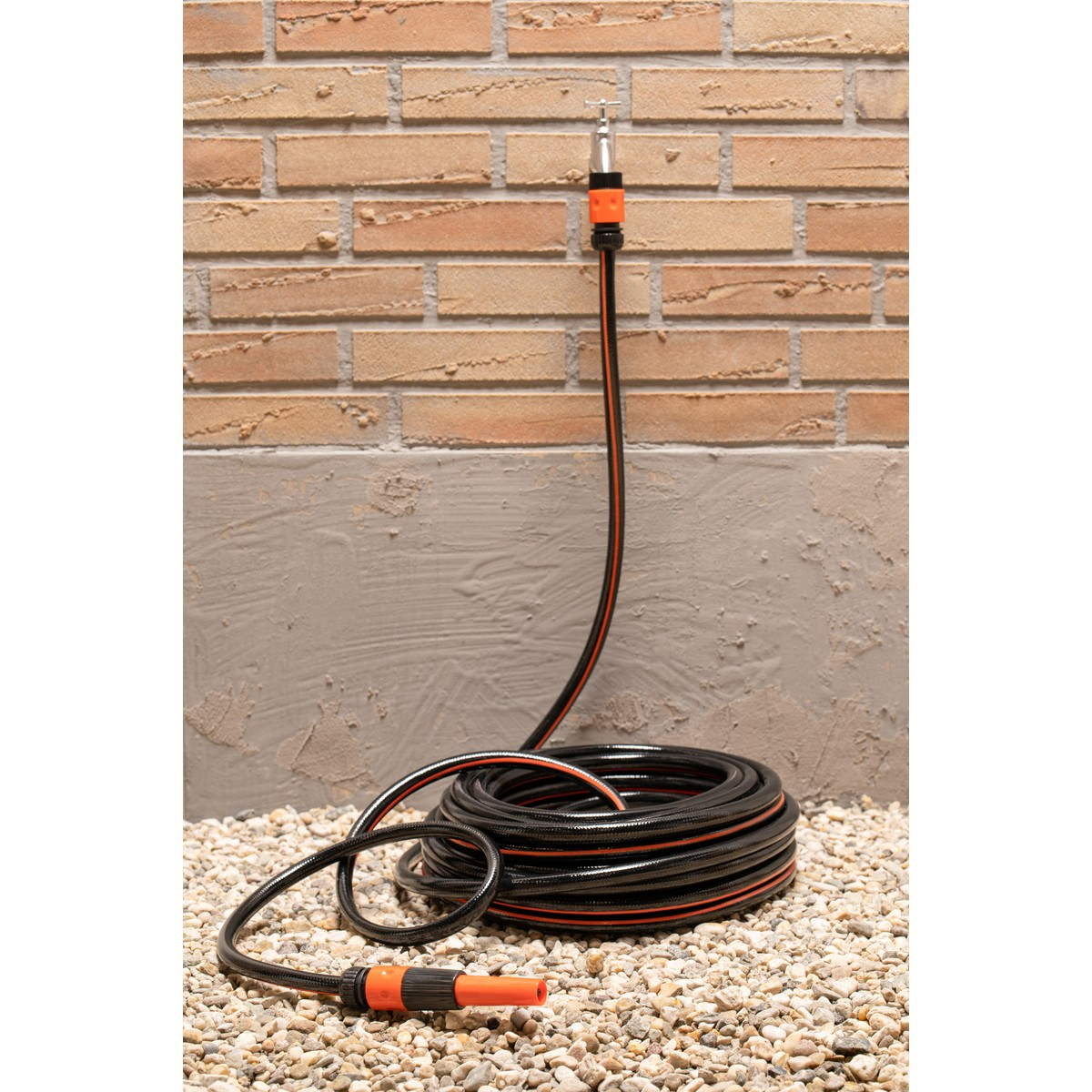 Black garden hose with orange stripes, coiled on pebbles.