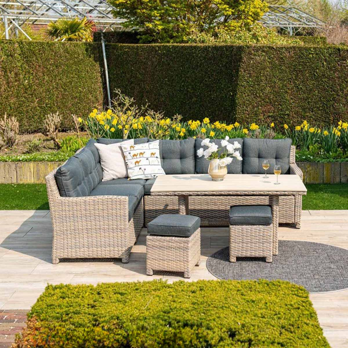 A rattan sofa with cushions and a table with flowers and glasses.