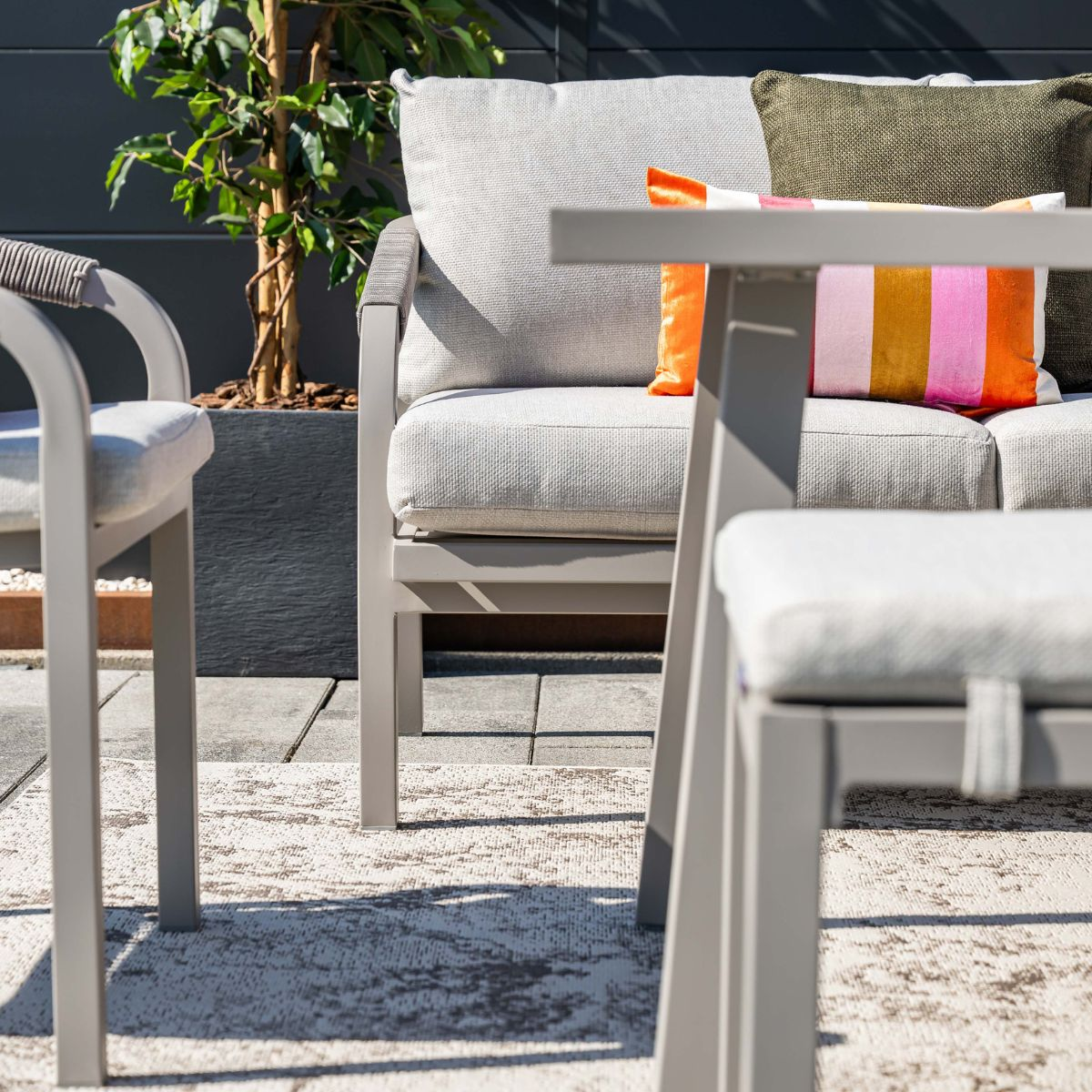 Gray outdoor furniture with colorful pillows and a plant.
