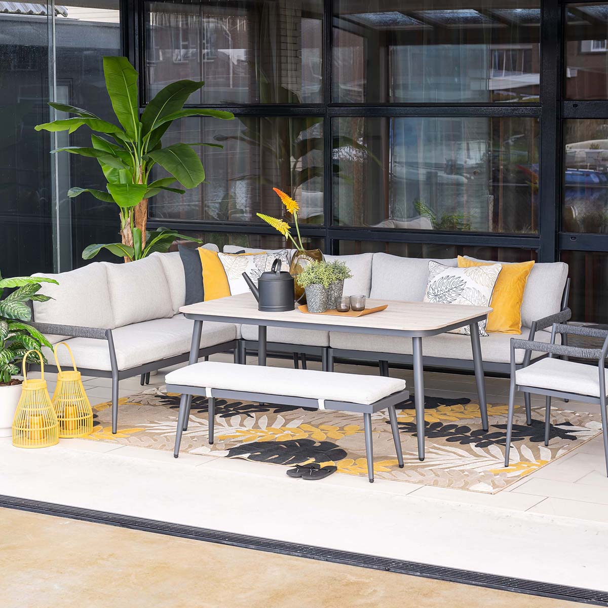 A modern outdoor lounge with a table, sofa, bench, and chairs on a rug.