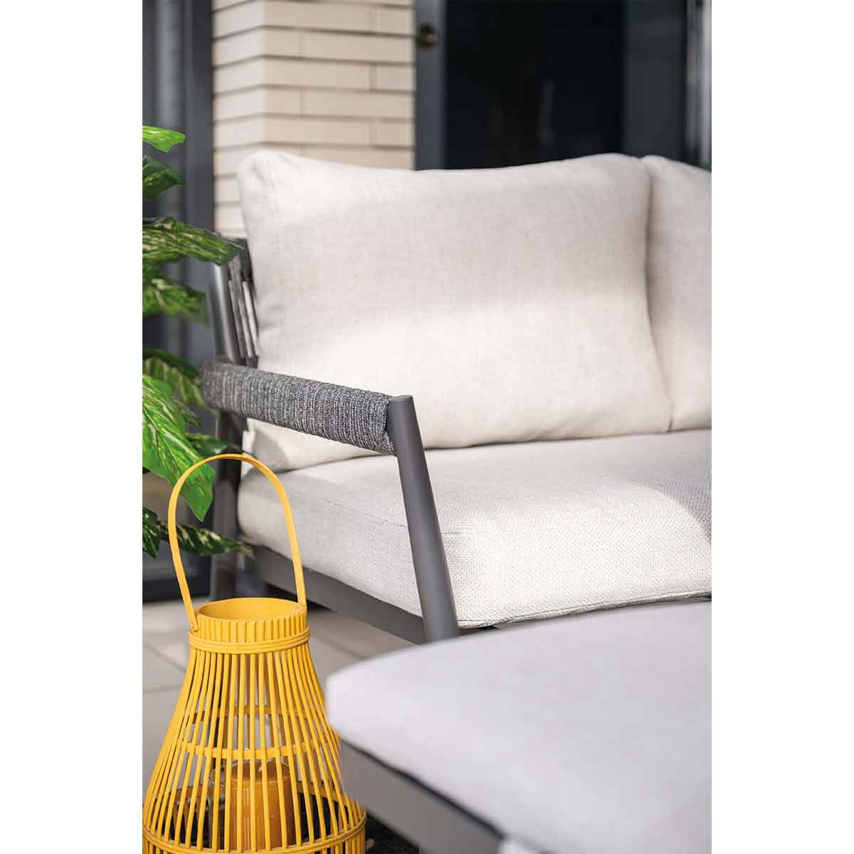 A yellow lantern stand sits next to a grey sofa with white cushions.