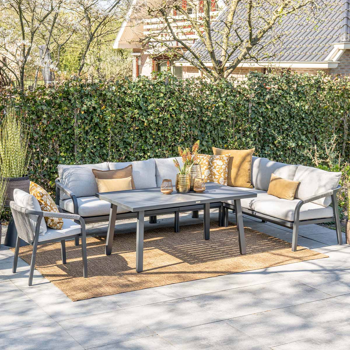 Een grijze loungeset met tafel staat op een terras voor een heg.