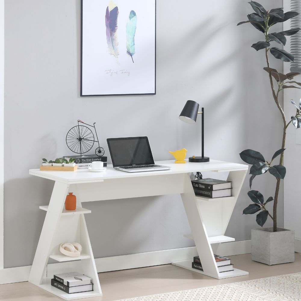 Una scrivania bianca con laptop, lampada, decorazioni e libri, accanto a una pianta.