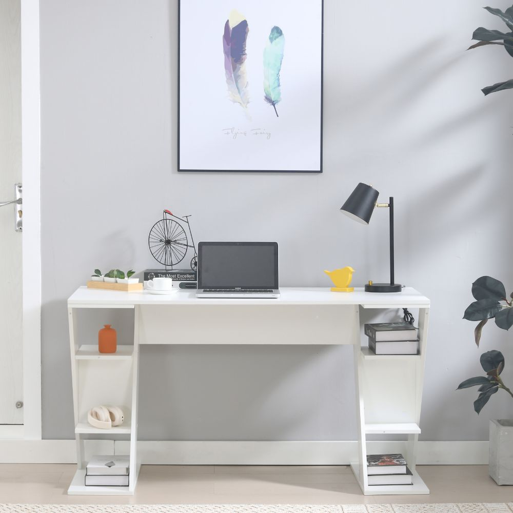 Una scrivania bianca con laptop, lampada, libri e decorazioni.