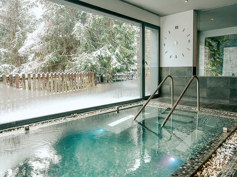 Piscina interior con vistas a un bosque nevado y valla de madera.