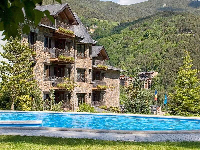 Edificio de piedra con balcones con vistas a una piscina azul brillante y colinas verdes.
