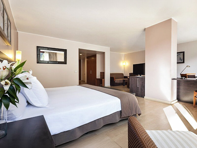 Un dormitorio con una cama grande, escritorio y zona de estar con lirios.