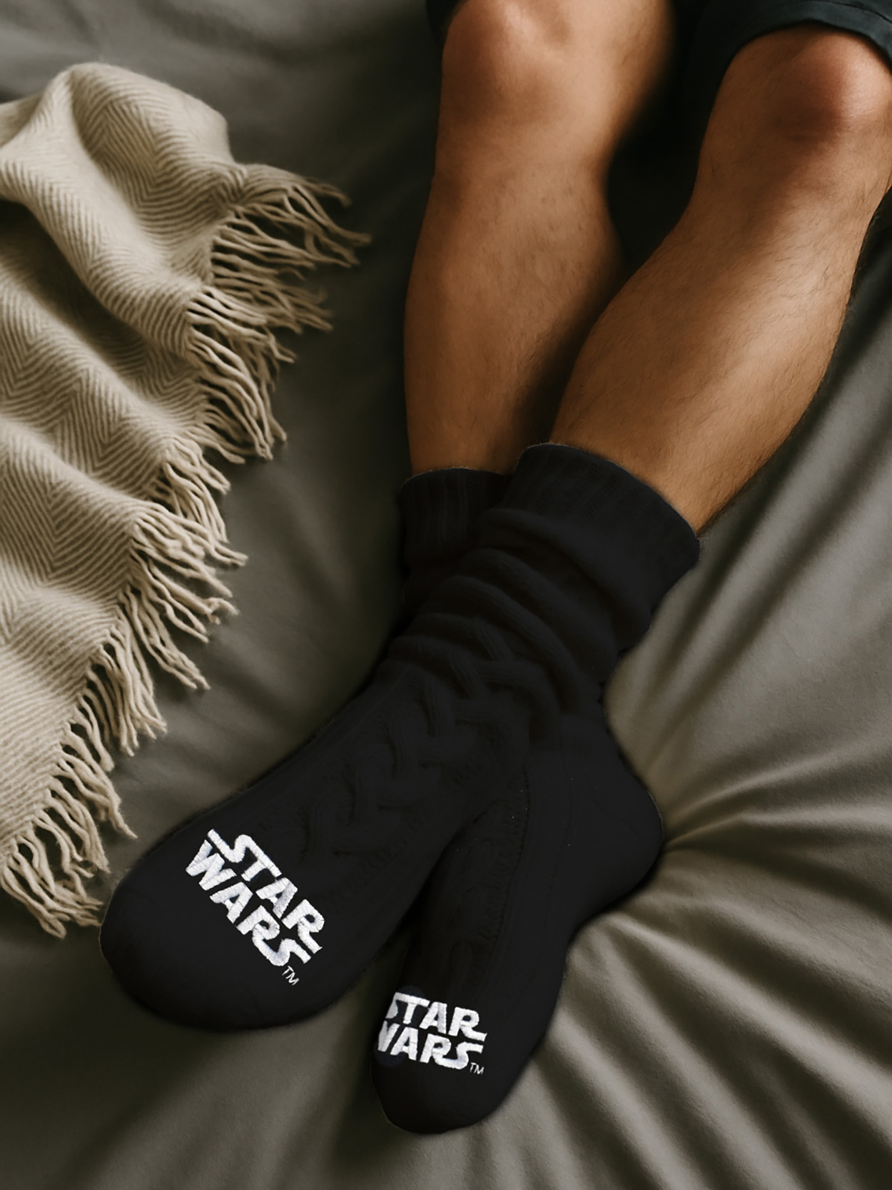 Schwarze Star Wars Socken mit weißem Logo auf einem Bett mit Decke.