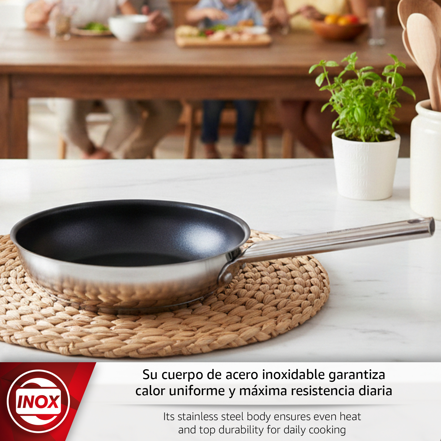 Sartén de acero inoxidable sobre mantel con familia al fondo.