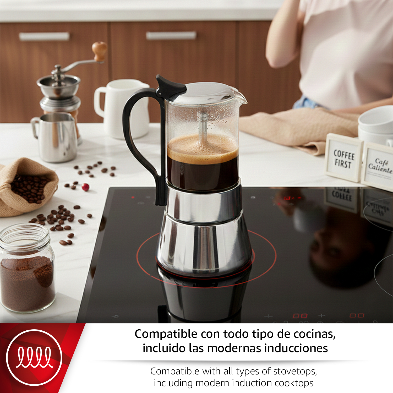 Cafetera sobre placa de inducción negra, con granos de café y jarra de leche cerca.