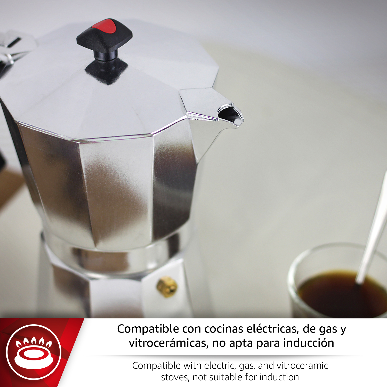 Cafetera plateada con asa negra y detalle rojo, junto a un vaso de café.